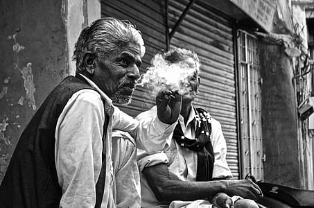 man smoking near man sitting at store front thumbnail