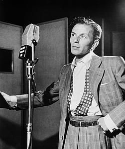 grayscale photo of man standing near condensing microphone thumbnail