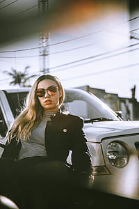 woman wearing black jacket and white striped shirt sitting behind white vehicle thumbnail