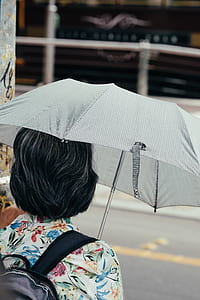 woman under gray umbrella standing beside gray post thumbnail