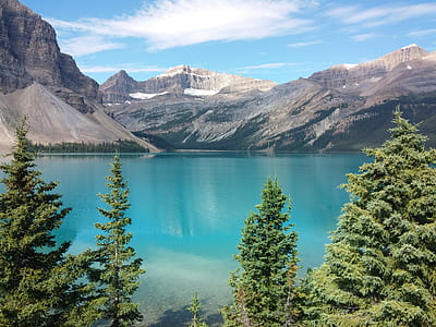 gray rocky mountain near body of water and pine trees during daytime thumbnail