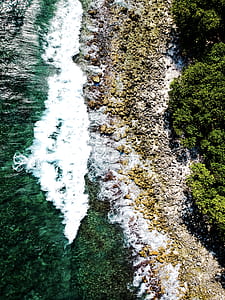 high angle photo of beach waves near trees and rocks thumbnail