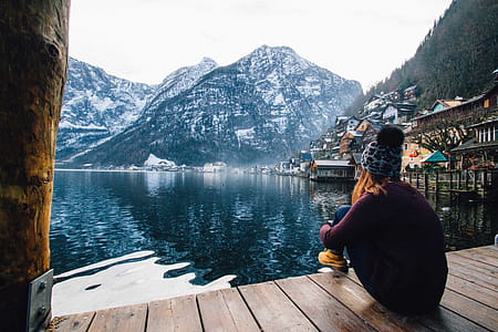Woman in Purple Sweater Sitting on Wooden Floor With View of Lake and Mountains thumbnail