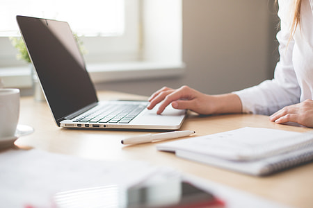 woman in white long-sleeved shirt holding gray laptop computer on brown wooden desk thumbnail