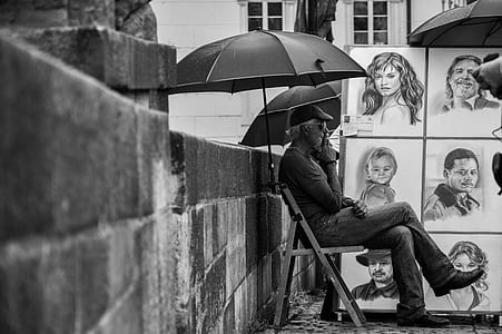 grayscale photo of man sitting on folding chair under umbrella thumbnail