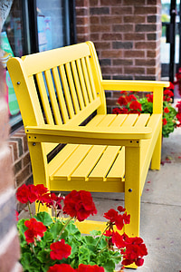 red potted geranium flowers beside yellow wooden bench thumbnail