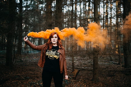woman wearing brown jacket holding smoke grenade while standing at the forest thumbnail