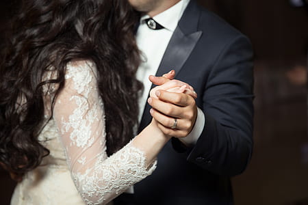 man wearing black peak lapel suit jacket and woman wearing white lace long-sleeved dress holding hands while dancing thumbnail