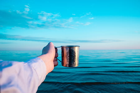 person holding stainless steel mug above ocean thumbnail