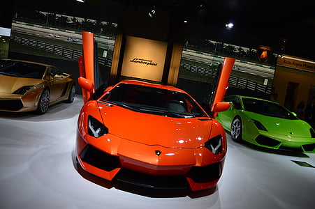 three orange, yellow, and green Lamborghini Aventador coupes parked on pavement thumbnail