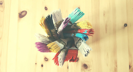 macro shot of assorted paint brushes placed on clear glass container on brown wooden surface thumbnail