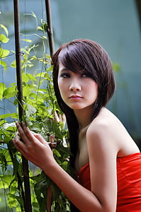 woman wearing red strapless top touching brown stick with green leaves at daytime thumbnail