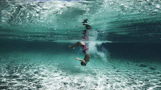 person swimming in the water near white sand thumbnail