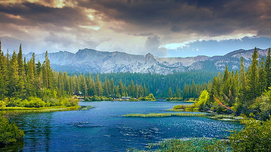 body of water along trees with snow-capped mountain at distance thumbnail