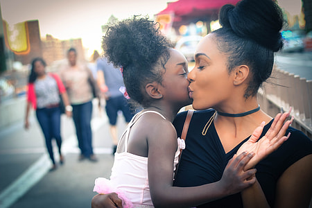 mother kissing her daughter in cheek while sitting beside the street during daytime thumbnail
