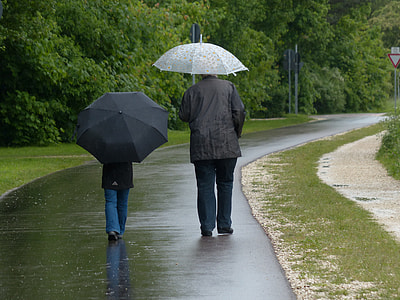 two person walking on pathway holding  open umbrella during rainy day thumbnail