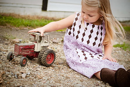 girl in white and purple sleeveless dress playing red and white toy car at daytime thumbnail
