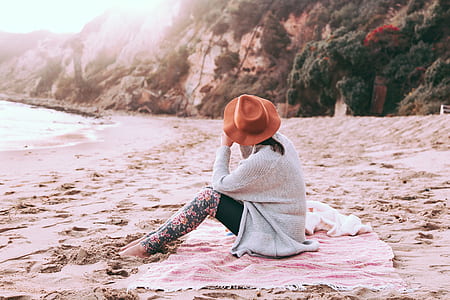 woman sitting on pink shawl near body of water thumbnail