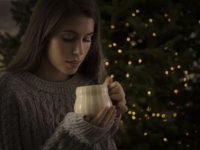 woman in gray knitted sweater holding white ceramic mug near Christmas tree thumbnail