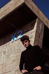 man in black long-sleeved top standing beside gray K2 concrete building thumbnail