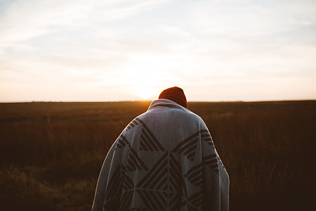 person covered by gray and black blanket facing sunrise thumbnail