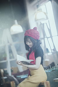 smiling woman reading book while sitting on sofa chair thumbnail