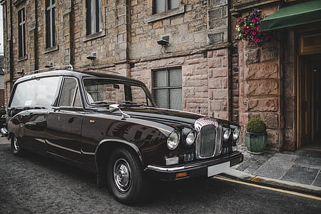 classic black vehicle parked beside brown concrete building at daytime thumbnail