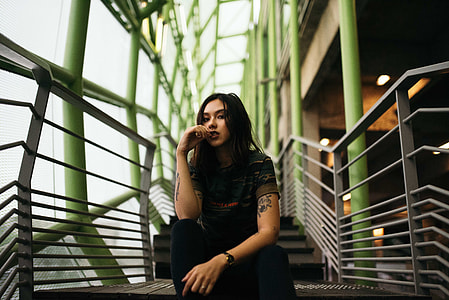 woman in black crew-neck shirt sitting on gray steel stairs indoors in shallow focus photography thumbnail