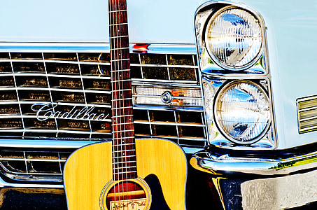 brown acoustic guitar leaning on white Cadillac car thumbnail