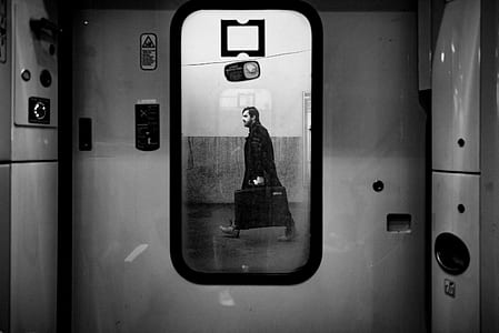grayscale photo of window with the view of man carrying luggage bag thumbnail