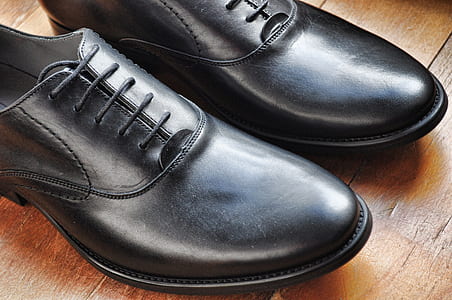 pair of black leather dress shoes on brown wooden panel thumbnail