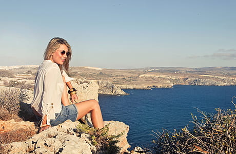 A young blonde wearing casuals with bracelets sitting on a rock by the sea thumbnail