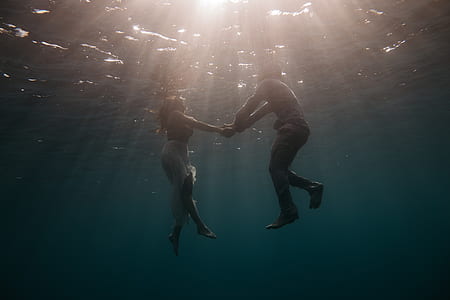 man and woman holding hand while floating on water thumbnail