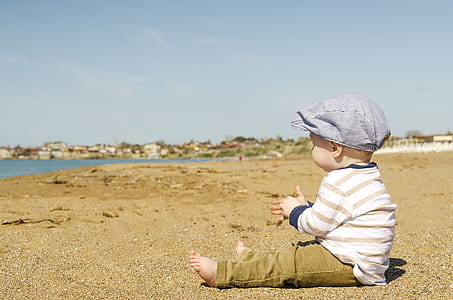 baby in white and brown striped long-sleeved shirt and pants outfit sitting on brown sand at daytime thumbnail