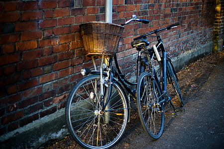 Two Black Bikes Parked Upright Beside Red Bricked Building thumbnail