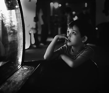 grayscale photo of boy leaning on wooden desk thumbnail
