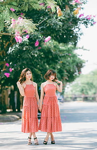 two women wearing same dress standing near green trees thumbnail