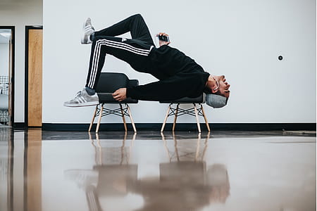 man lying on two stools near white wall inside well lit room thumbnail