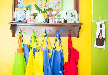 assorted-color aprons hanging on pegs on wall thumbnail