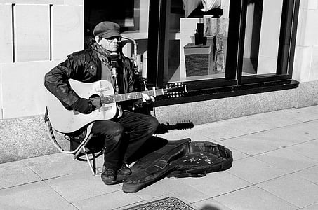 grayscale photo of man playing guitar sitting on chair thumbnail
