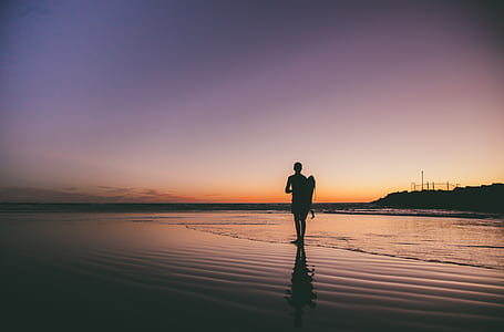 silhouette photo of man standing seashore during golden hour thumbnail