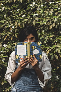 woman standing near green leafed plants while holding a book thumbnail