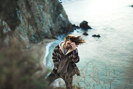 man holding his forehead while standing on mountain beside body of water thumbnail