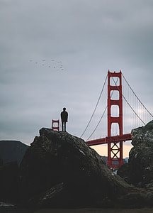 silhouette photo of a man on rock formation facing London Bridge during daytime thumbnail