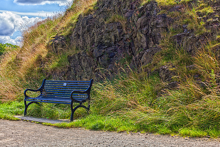 black patio bench on grasses against rock thumbnail