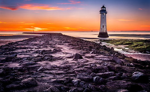 photo of lighthouse surrounding body of water during golden hour thumbnail
