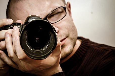man in black framed eyeglasses using black Nikon DSLR camera thumbnail