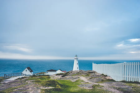 white lighthouse and two houses inside the fence with wide body of water in distance thumbnail