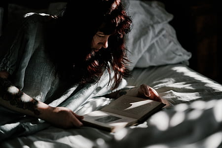 woman lying on bed while reading book thumbnail