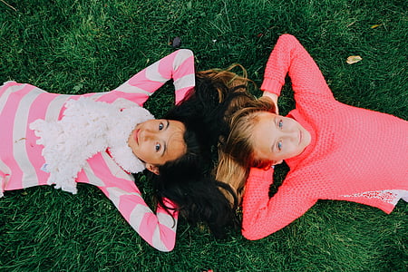 two girls wearing pink and white long-sleeved shirts lying on grass during daytime thumbnail